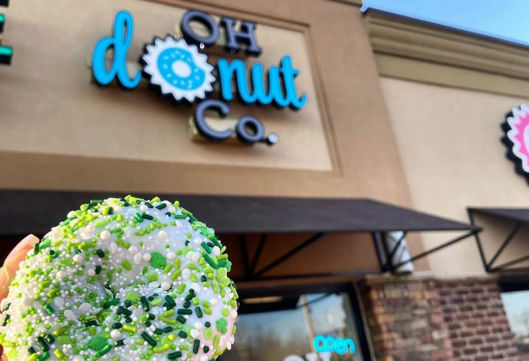 Donut held up in front of OH Donut Co. storefront.