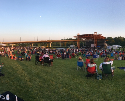 People sitting on the grassy lawn at The Youngstown Foundation Amphitheatre during a concert.